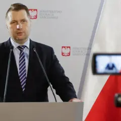 Mężczyzna w garniturze przemawia przy mównicy na tle flagi Polski i logo Ministerstwa Edukacji Narodowej.