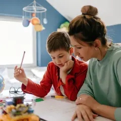 Kobieta i chłopiec uczący się przy biurku z globusem i kredkami.