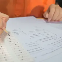 Dłoń z ołówkiem zaznacza odpowiedzi na arkuszu egzaminacyjnym.