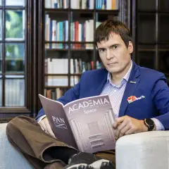 Mężczyzna w niebieskiej marynarce siedzi w fotelu i czyta magazyn "Academia Space".
