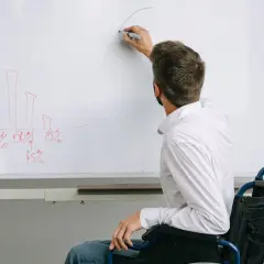Mężczyzna na wózku inwalidzkim pisze na tablicy wykres słupkowy i krzywą.