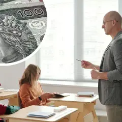 Zbliżenie na polskie banknoty 100 zł i nauczyciela prowadzącego lekcję dla uczniów.