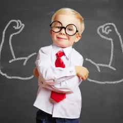 Uśmiechnięty chłopiec w okularach i krawacie na tle tablicy z rysunkami bicepsów.