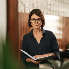 Kobieta w okularach trzymająca otwarty notatnik.
