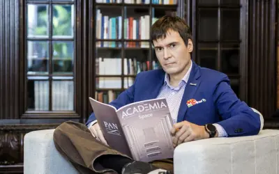 Mężczyzna w niebieskiej marynarce siedzi w fotelu i czyta magazyn "Academia Space".