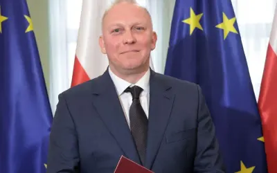 Tomasz Szabłowski w garniturze, na tle flag Polski i Unii Europejskiej.