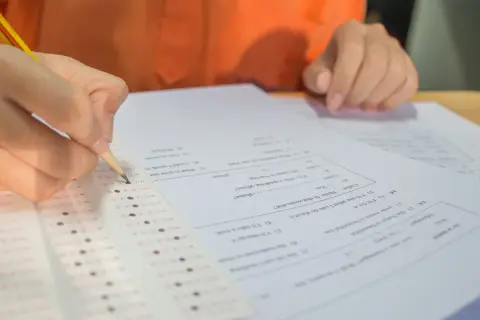 Dłoń z ołówkiem zaznacza odpowiedzi na arkuszu egzaminacyjnym.