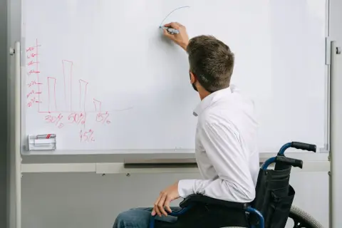 Mężczyzna na wózku inwalidzkim pisze na tablicy wykres słupkowy i krzywą.