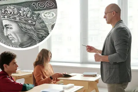 Zbliżenie na polskie banknoty 100 zł i nauczyciela prowadzącego lekcję dla uczniów.