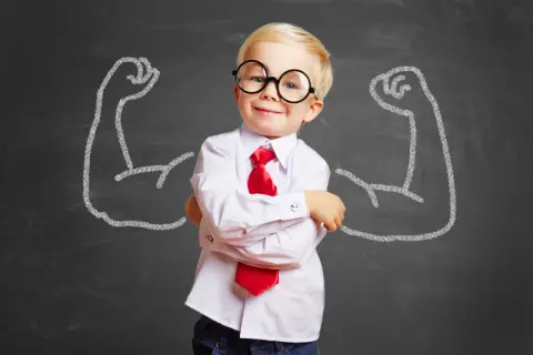 Uśmiechnięty chłopiec w okularach i krawacie na tle tablicy z rysunkami bicepsów.