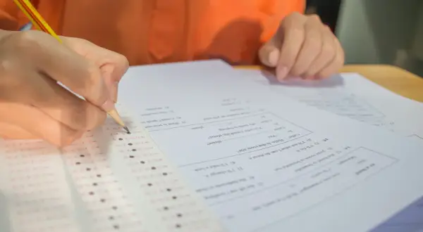 Dłoń z ołówkiem zaznacza odpowiedzi na arkuszu egzaminacyjnym.