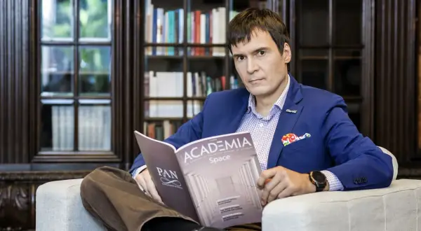 Mężczyzna w niebieskiej marynarce siedzi w fotelu i czyta magazyn "Academia Space".