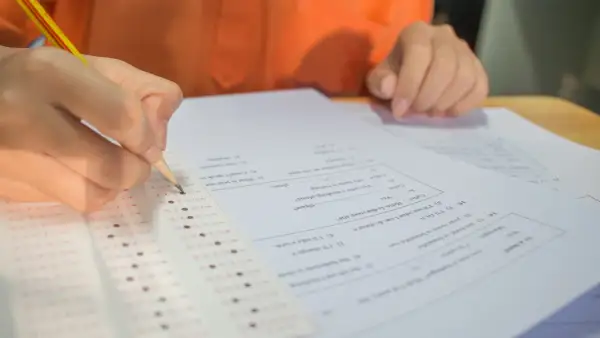Dłoń z ołówkiem zaznacza odpowiedzi na arkuszu egzaminacyjnym.