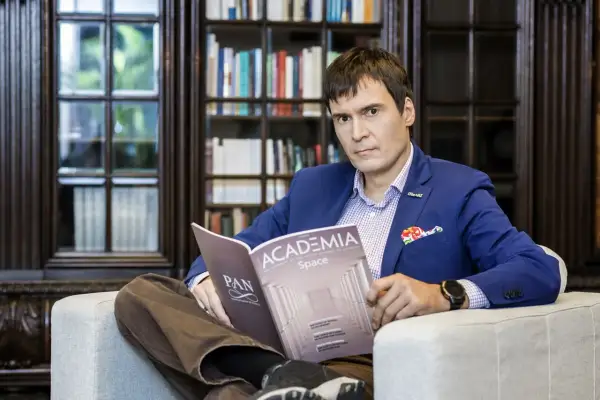 Mężczyzna w niebieskiej marynarce siedzi w fotelu i czyta magazyn "Academia Space".