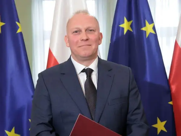 Tomasz Szabłowski w garniturze, na tle flag Polski i Unii Europejskiej.